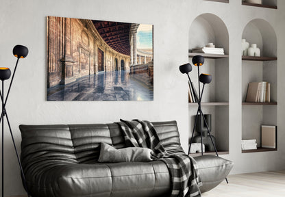 Glass wall art depicting a sunlit classical colonnade with ornate architecture displayed above a gray leather sofa in a modern living room.