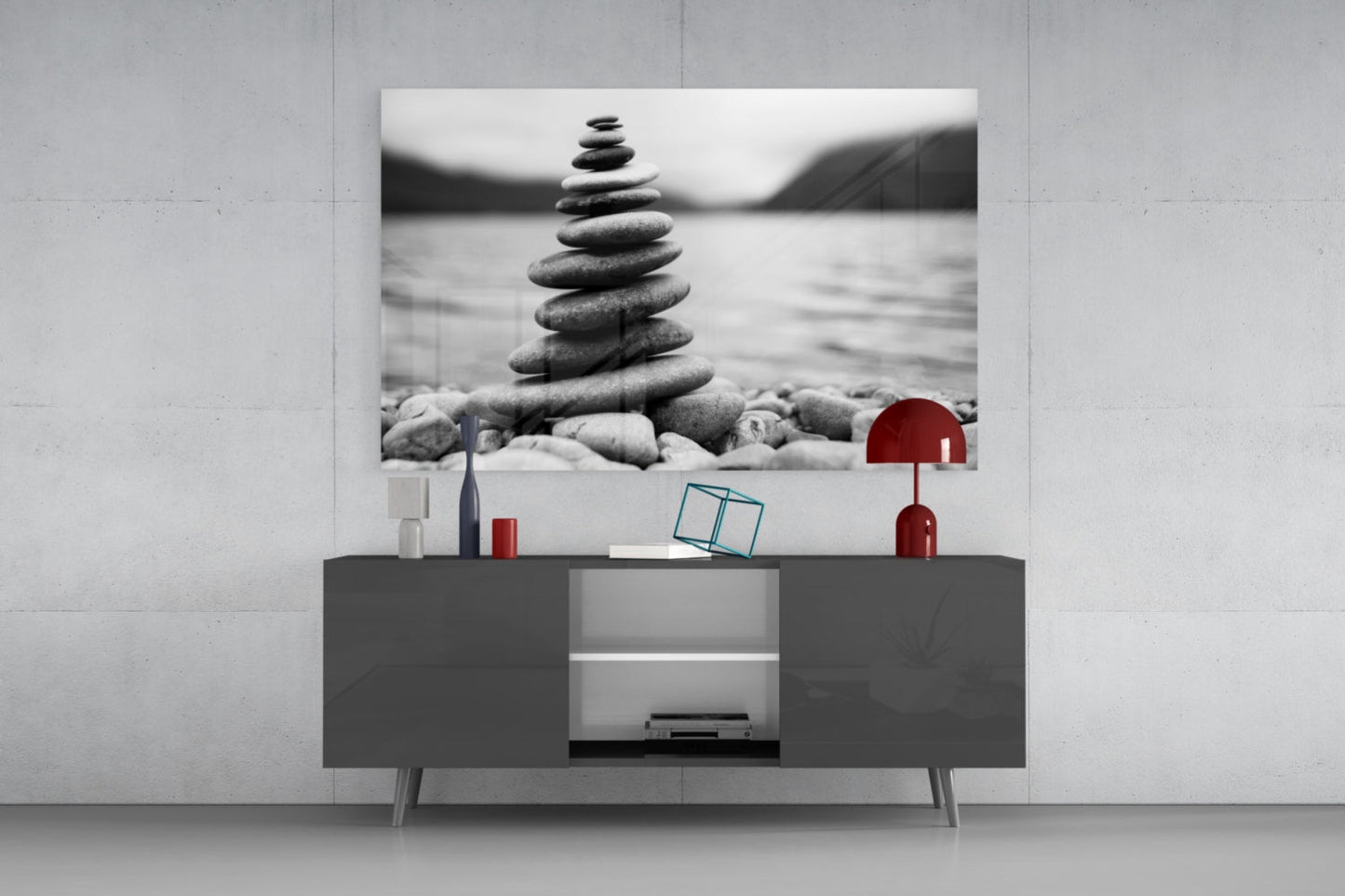 Black and white stacked pebbles artwork displayed above gray TV console with red lamp and decorative objects.