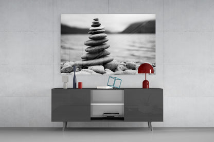 Black and white stacked pebbles artwork displayed above gray TV console with red lamp and decorative objects.