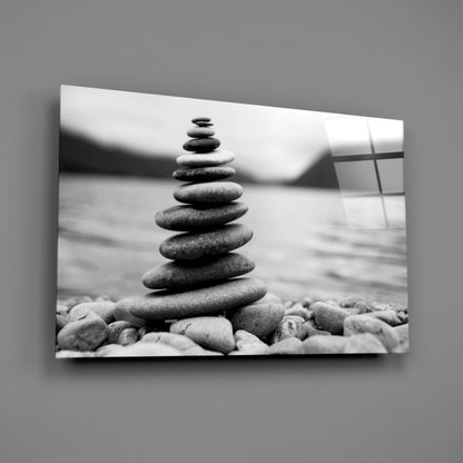 Stacked smooth pebbles in black and white on a pebbly beach with blurred water and sky background.