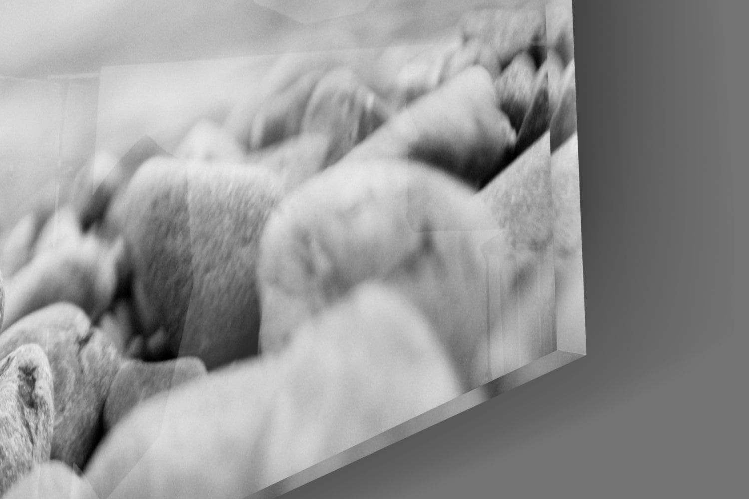 Close-up angled view of smooth gray and white pebbles with soft shadows and texture detail on glass surface.