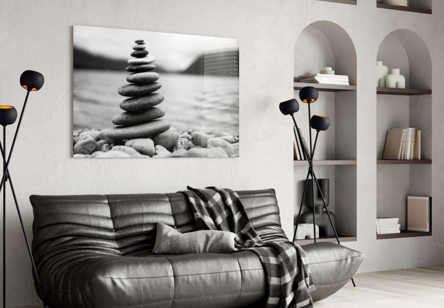 Stacked stones balanced on a beach in black and white photograph displayed above a dark leather sofa in a minimalist living room.