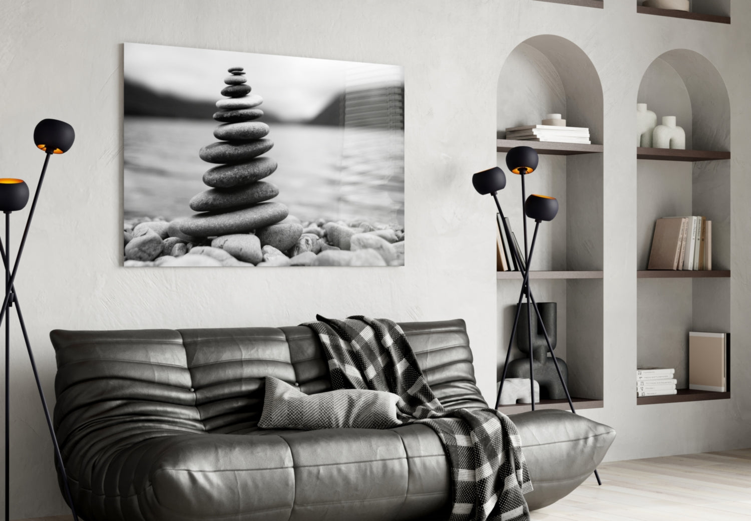 Stacked stones balanced on a beach in black and white photograph displayed above a dark leather sofa in a minimalist living room.