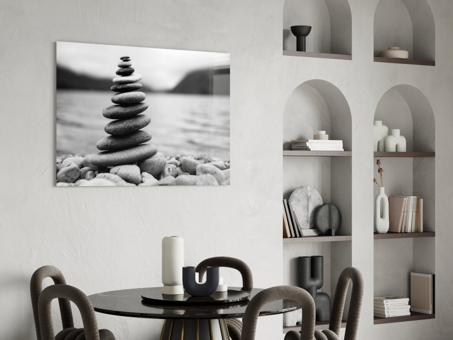 Stacked pebbles balanced on a beach in monochrome glass wall art hung above a round black dining table with upholstered chairs.