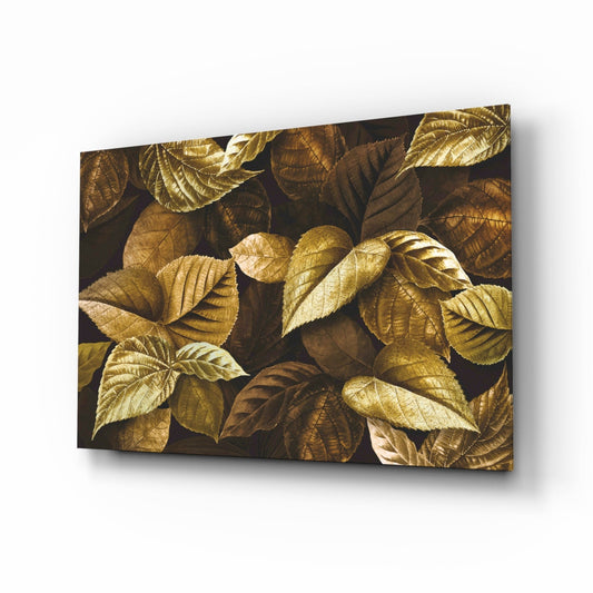 Glass wall art panel displaying metallic gold and bronze leaves on dark background, angled perspective view with shadow cast.