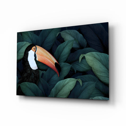 Angled view of glass wall art featuring a toucan with black plumage and orange beak nestled among dark green foliage.