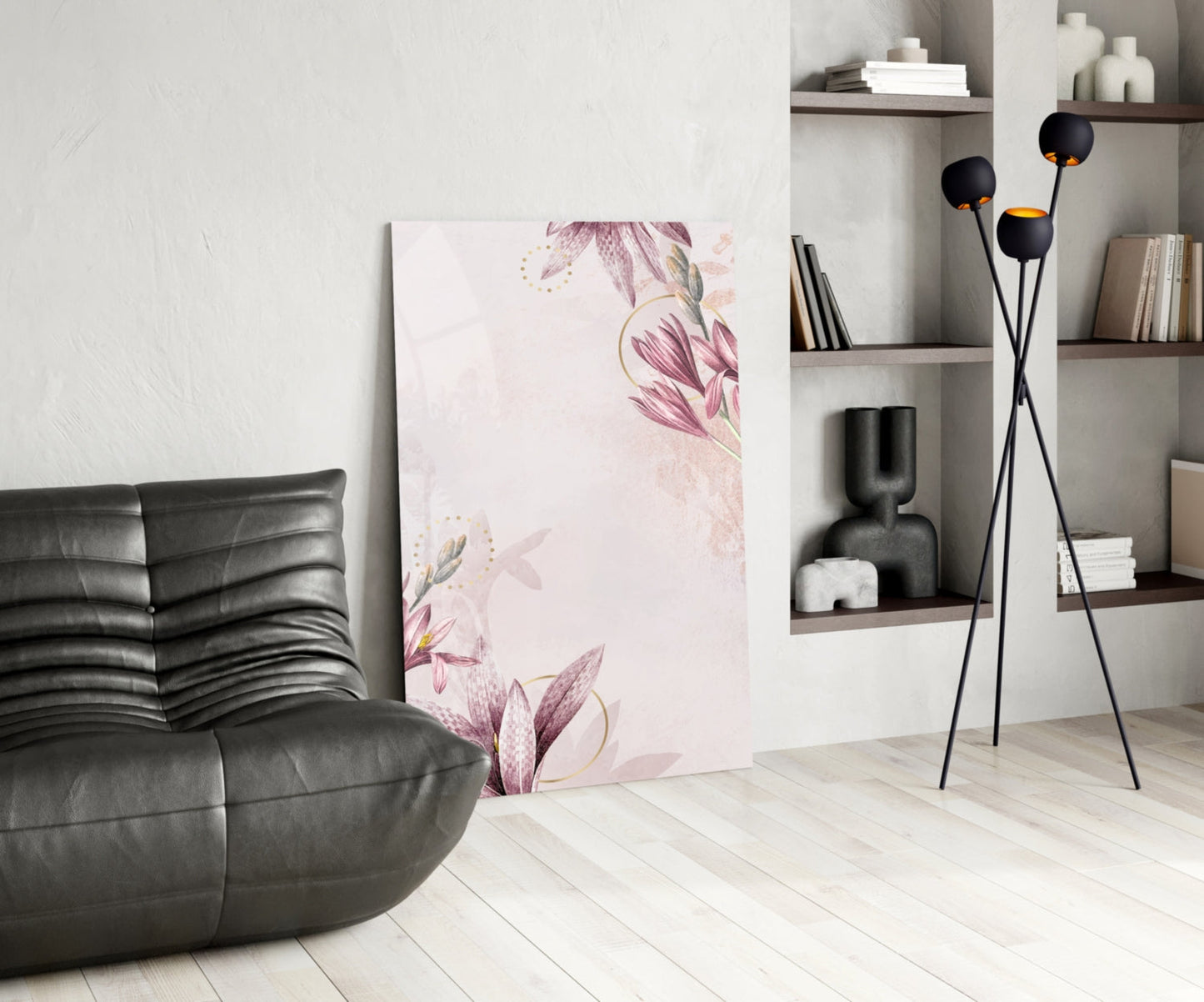 Pink floral glass wall art displayed leaning against white wall in modern living room with black leather chair and shelving.