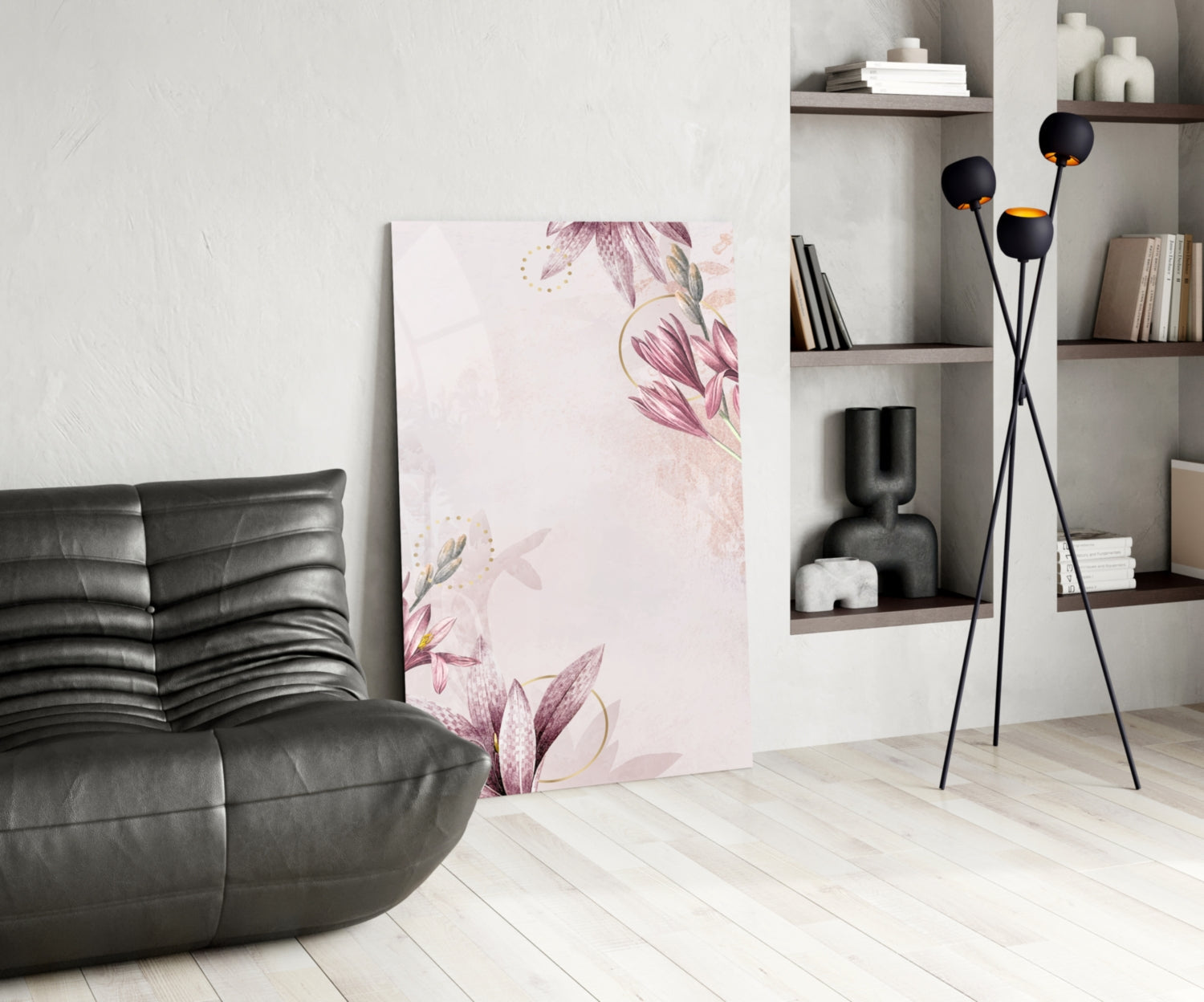Pink floral glass wall art displayed leaning against white wall in modern living room with black leather chair and shelving.