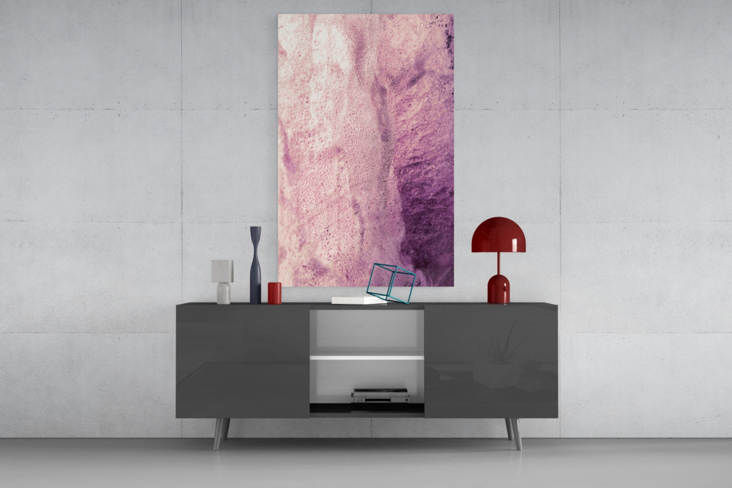 Pink abstract gradient glass art panel displayed above gray media console with red lamp and decorative accessories.