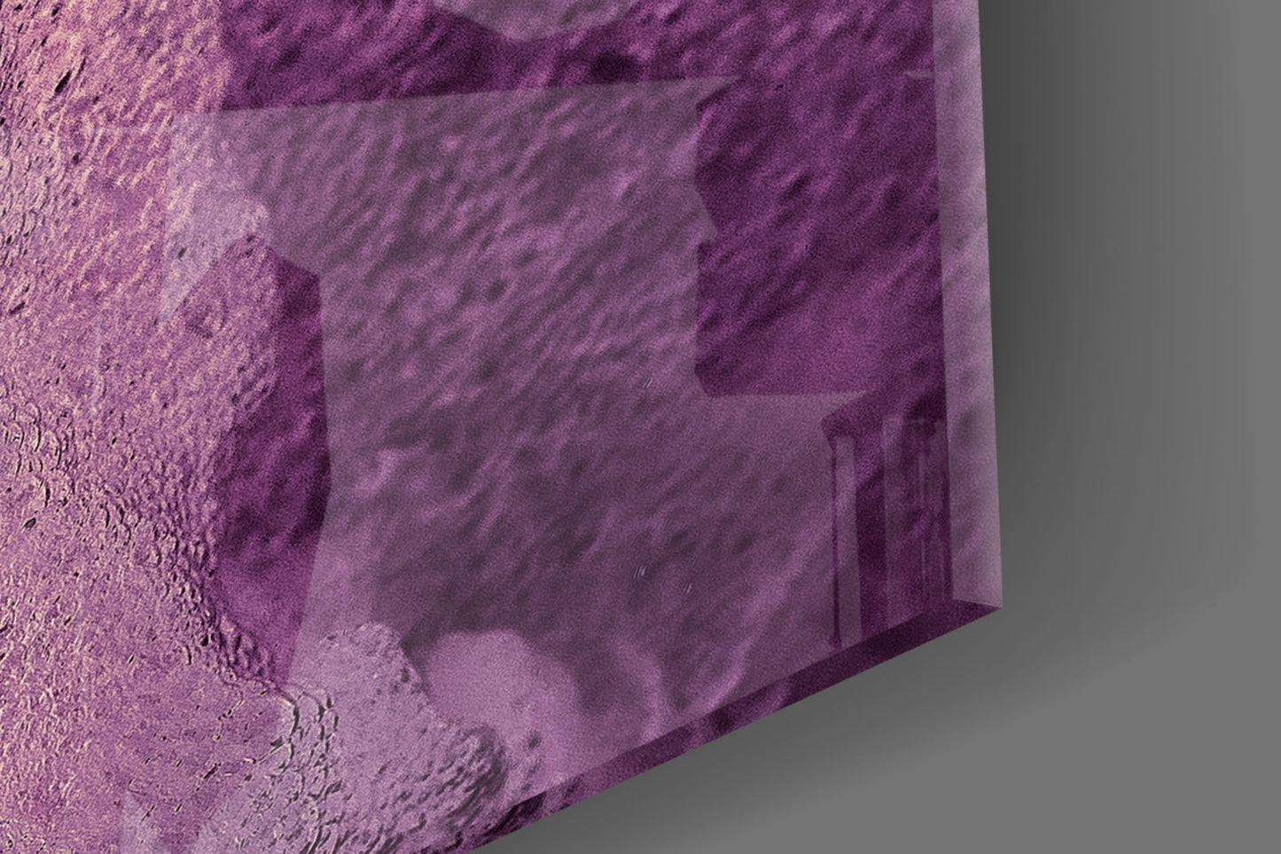 Close-up of purple abstract glass wall art edge showing textured surface and diagonal pattern details against gray background.
