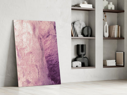 Pink and purple ombre abstract glass artwork leaning against white wall beside built-in shelving with decorative objects and books.