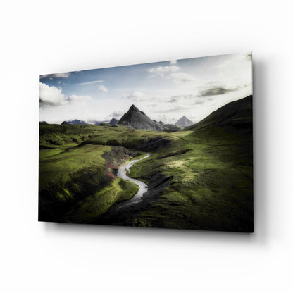 Angled view of glass wall art displaying a lush green valley with a winding river and dramatic peaked mountain in the background.