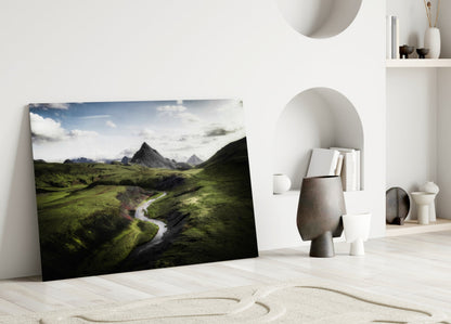 Green Valley Glass Wall Art leaning against white wall showing Icelandic landscape with green hills, river, and mountains.