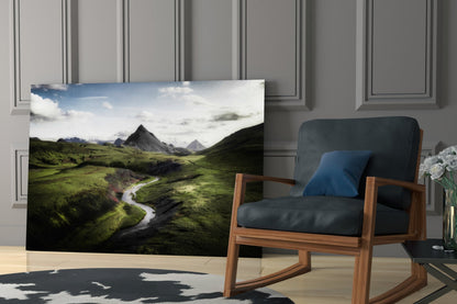 Glass wall art displaying lush green valley with winding river and mountains, displayed in modern interior with wooden chair.