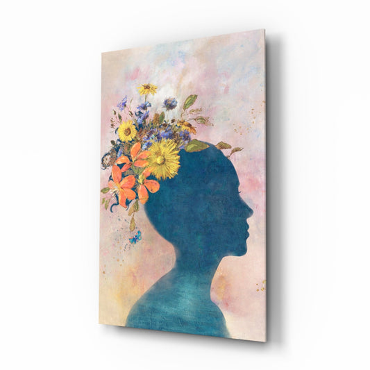 Blue silhouette profile with colorful flowers erupting from head, displayed at an angle on white background showing glass material and shadow.