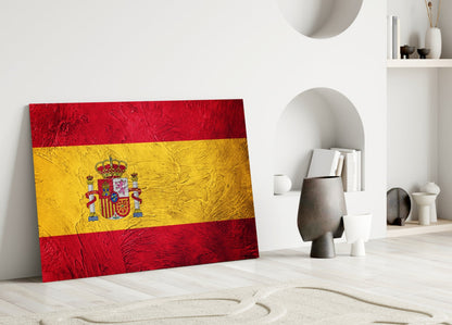 Spanish flag glass wall art leaning against white wall in minimalist interior with decorative objects and shelving.