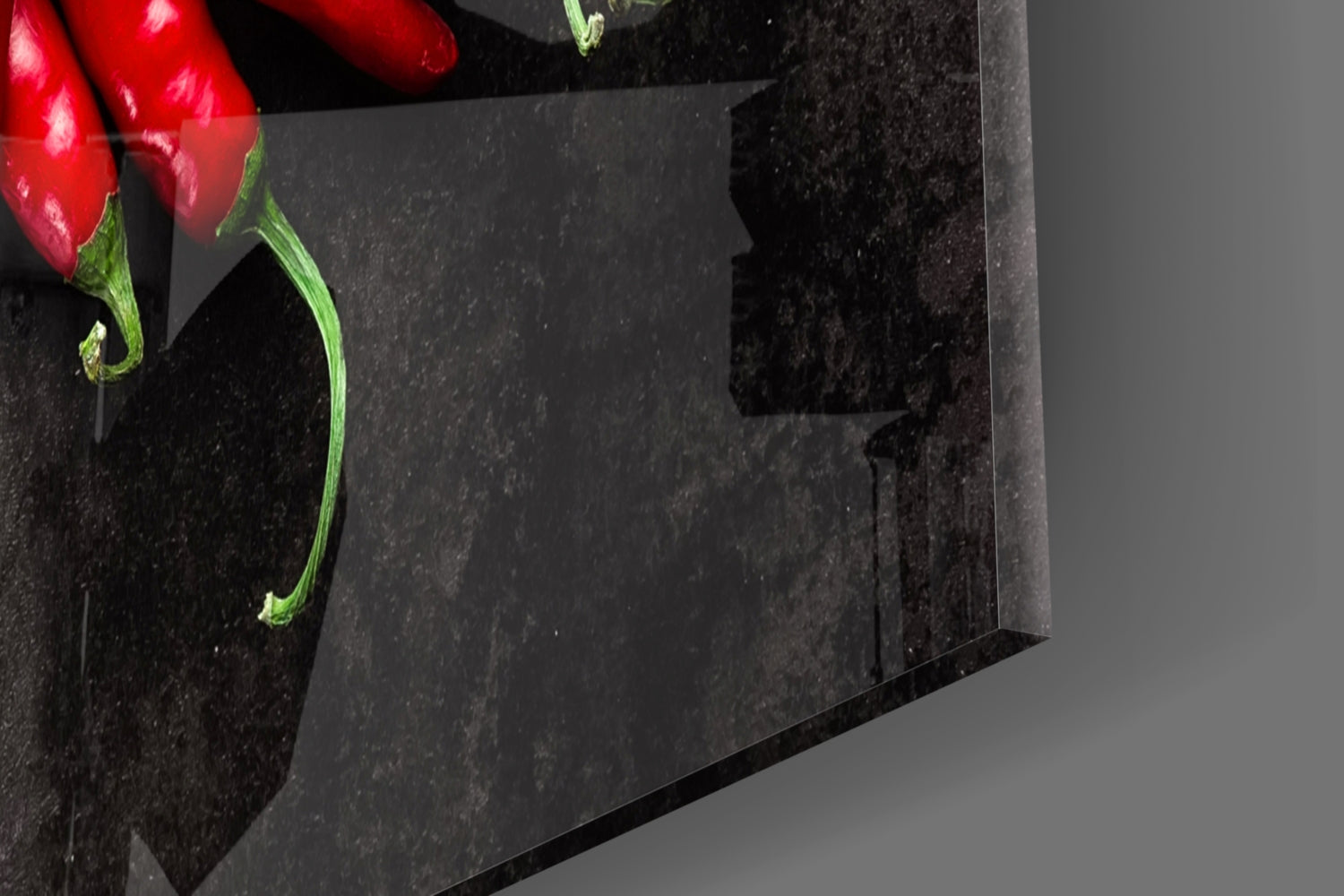 Close-up angled view of red peppers with green stems on black textured glass against gray background.