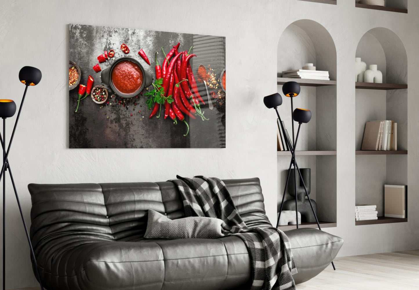 Red peppers glass wall art displayed above black leather sofa in modern living room with built-in shelving.