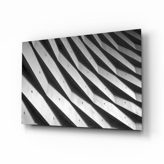 Black and white photograph of curved architectural ribbing with shadow striations and small circular holes, displayed as a tilted glass wall panel.