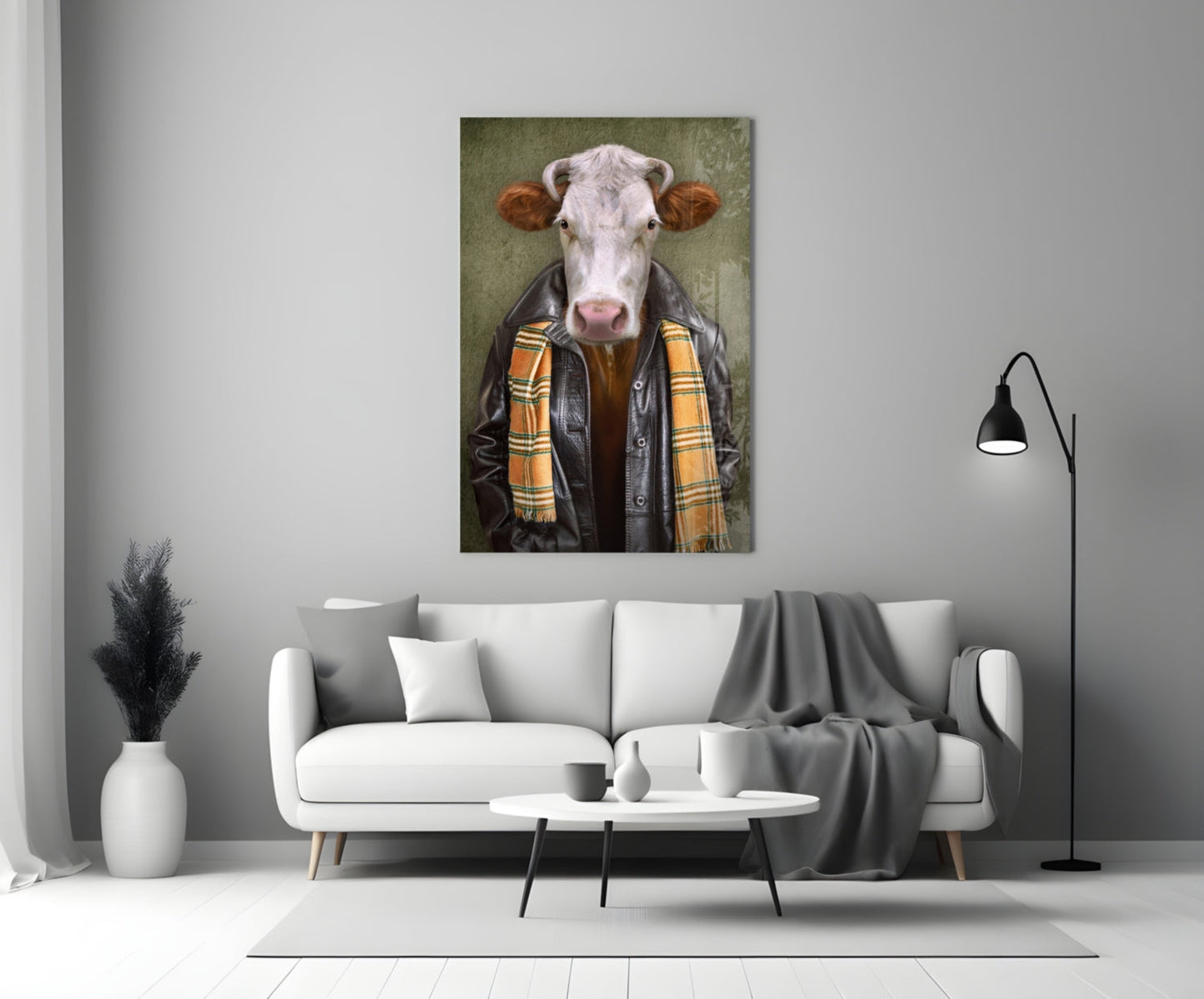 Glass wall art depicting a cow with white face and brown ears wearing a black leather jacket and yellow plaid scarf, displayed above a white sofa in a modern living room.