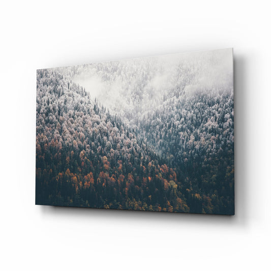 Angled view of glass wall art displaying misty forested mountain slopes with autumn foliage in brown and green tones fading into white mist.