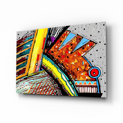 Angled view of colorful abstract glass wall art with geometric patterns, vibrant orange, yellow, blue, and red sections mounted on perforated metal backing.
