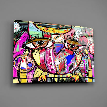 Colorful abstract glass wall art featuring two stylized owl faces with bold black outlines, vibrant magenta, yellow, blue, and pink geometric patterns throughout, displayed against a gray wall.