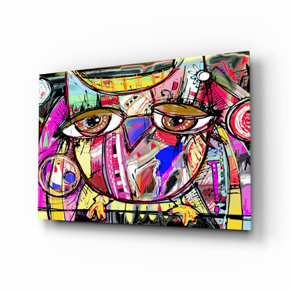 Angled view of a colorful abstract owl glass wall art with vibrant pink, yellow, blue, and black geometric patterns and bold brown eyes.