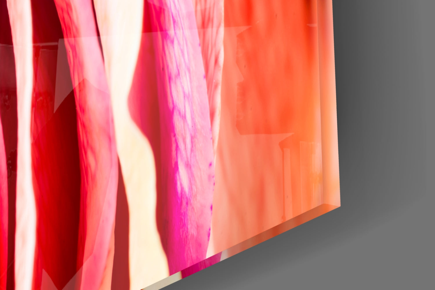 Angled close-up view of translucent colored glass sheets in red, pink, magenta, and orange tones against gray background.