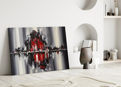 Modern interior display featuring abstract cityscape glass art with red, gray, and black tones leaning against white wall.
