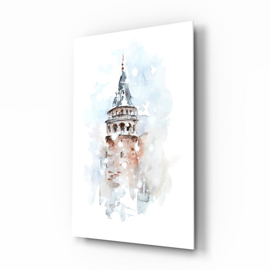 Angled view of glass wall art displaying a watercolor painting of Galata Tower in soft blue, beige, and terracotta tones on white background.