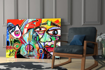 Colorful abstract glass wall art featuring vibrant red, yellow, blue, and green sections with expressive face designs displayed in modern room setting beside wooden rocking chair.