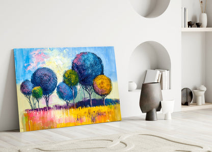 Colorful glass wall art leaning against white wall displays vibrant blue, pink, yellow trees in landscape scene.