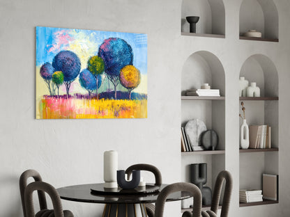 Colorful glass wall art depicting stylized trees with blue, yellow, and pink foliage displayed above a dining table in a modern interior.