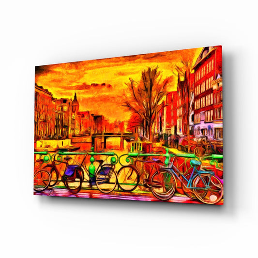Vibrant glass wall art displaying colorful bicycles lined against a railing with a dramatic golden sunset cityscape background.