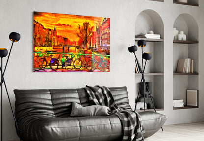 Vibrant glass wall art depicting colorful bicycles and orange sunset cityscape displayed above black leather sofa.