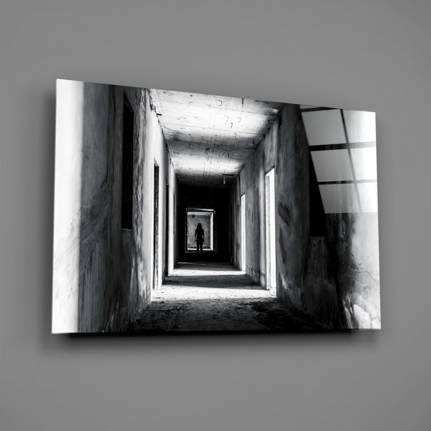 Black and white photograph of a lone silhouetted figure standing in a distant brightly lit doorway within a long concrete tunnel corridor.