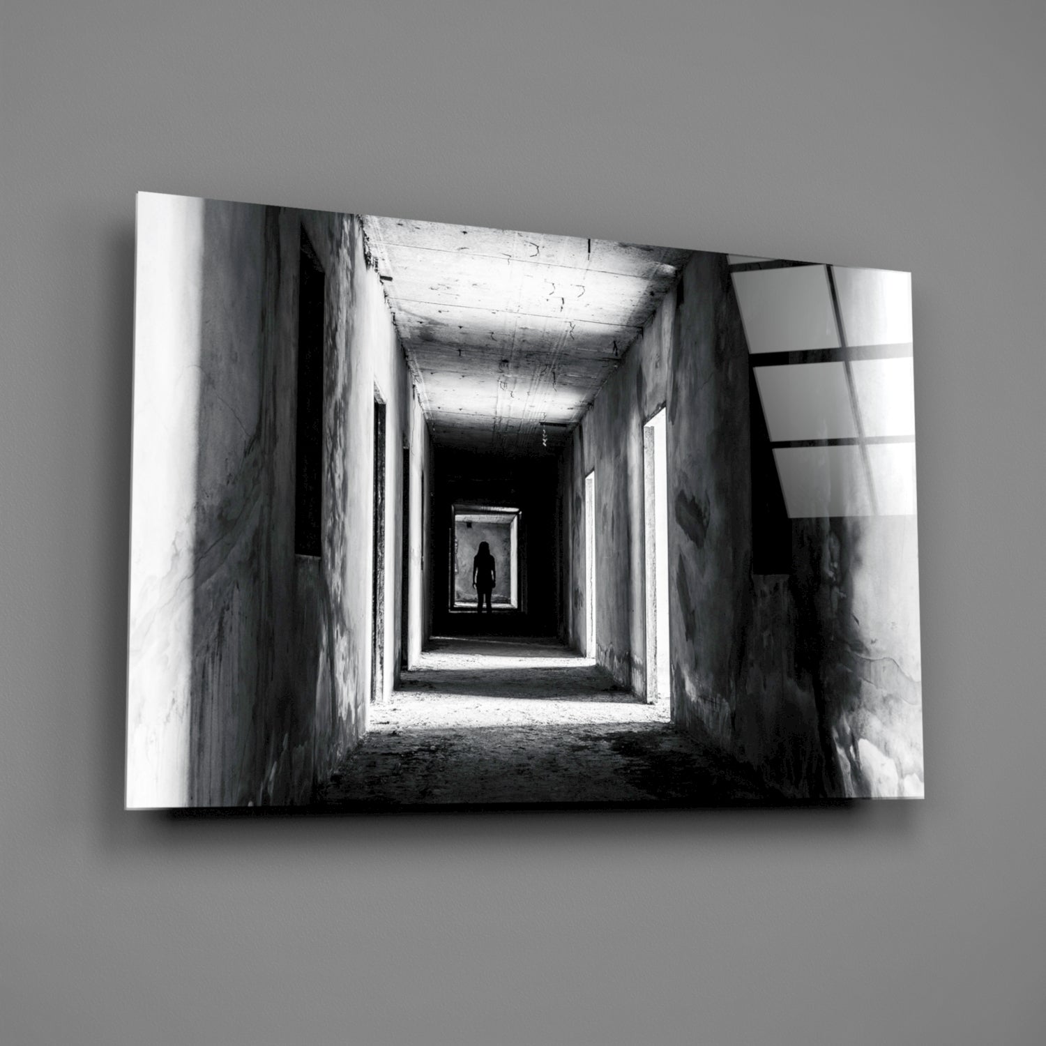 Black and white photograph of a lone silhouetted figure standing in a distant brightly lit doorway within a long concrete tunnel corridor.