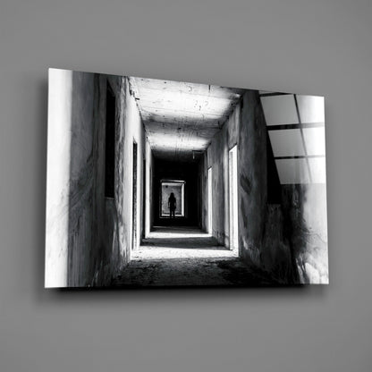 Black and white photograph of a lone silhouetted figure standing in a distant brightly lit doorway within a long concrete tunnel corridor.