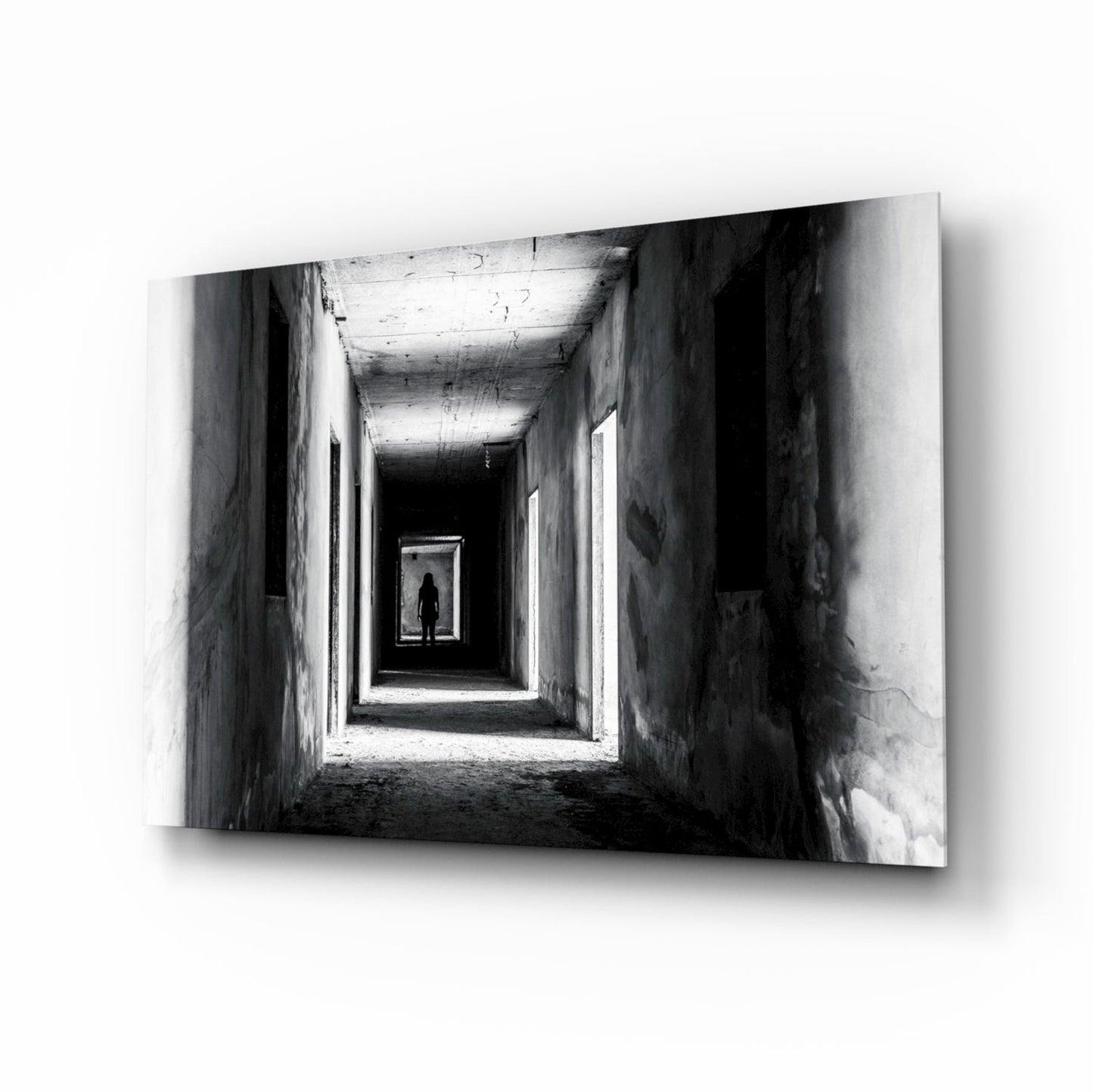 Black and white photograph of a silhouetted figure standing in a receding tunnel with concrete walls and overhead lighting.