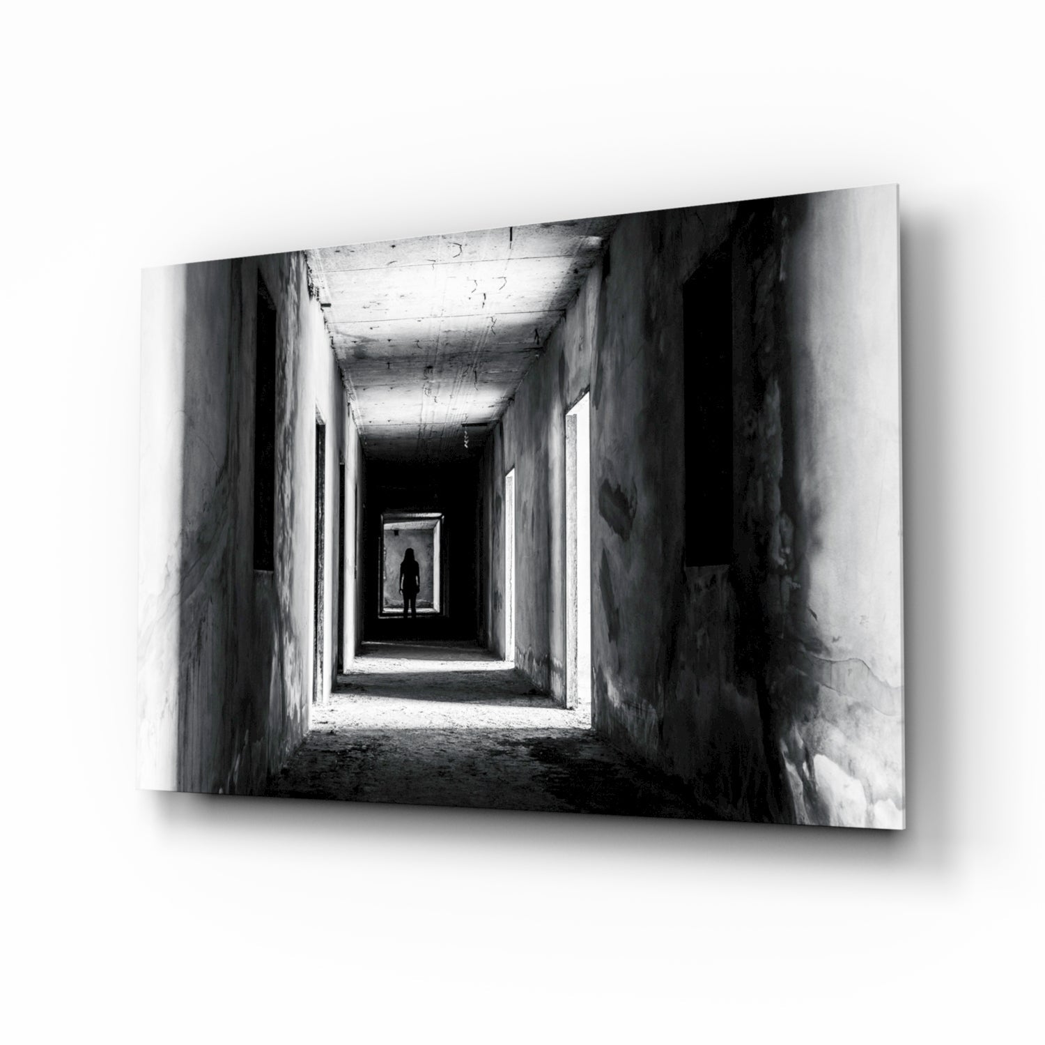 Black and white photograph of a silhouetted figure standing in a receding tunnel with concrete walls and overhead lighting.