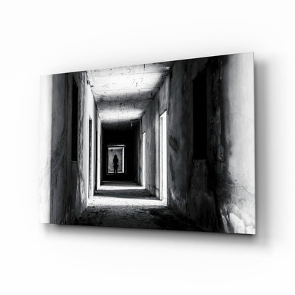 Black and white photograph of a silhouetted figure standing in a receding tunnel with concrete walls and overhead lighting.