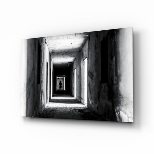 Black and white photograph of a silhouetted figure standing in a receding tunnel with concrete walls and overhead lighting.