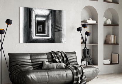 Black and white photograph of a receding illuminated corridor displayed above a gray leather sofa in a modern living room.