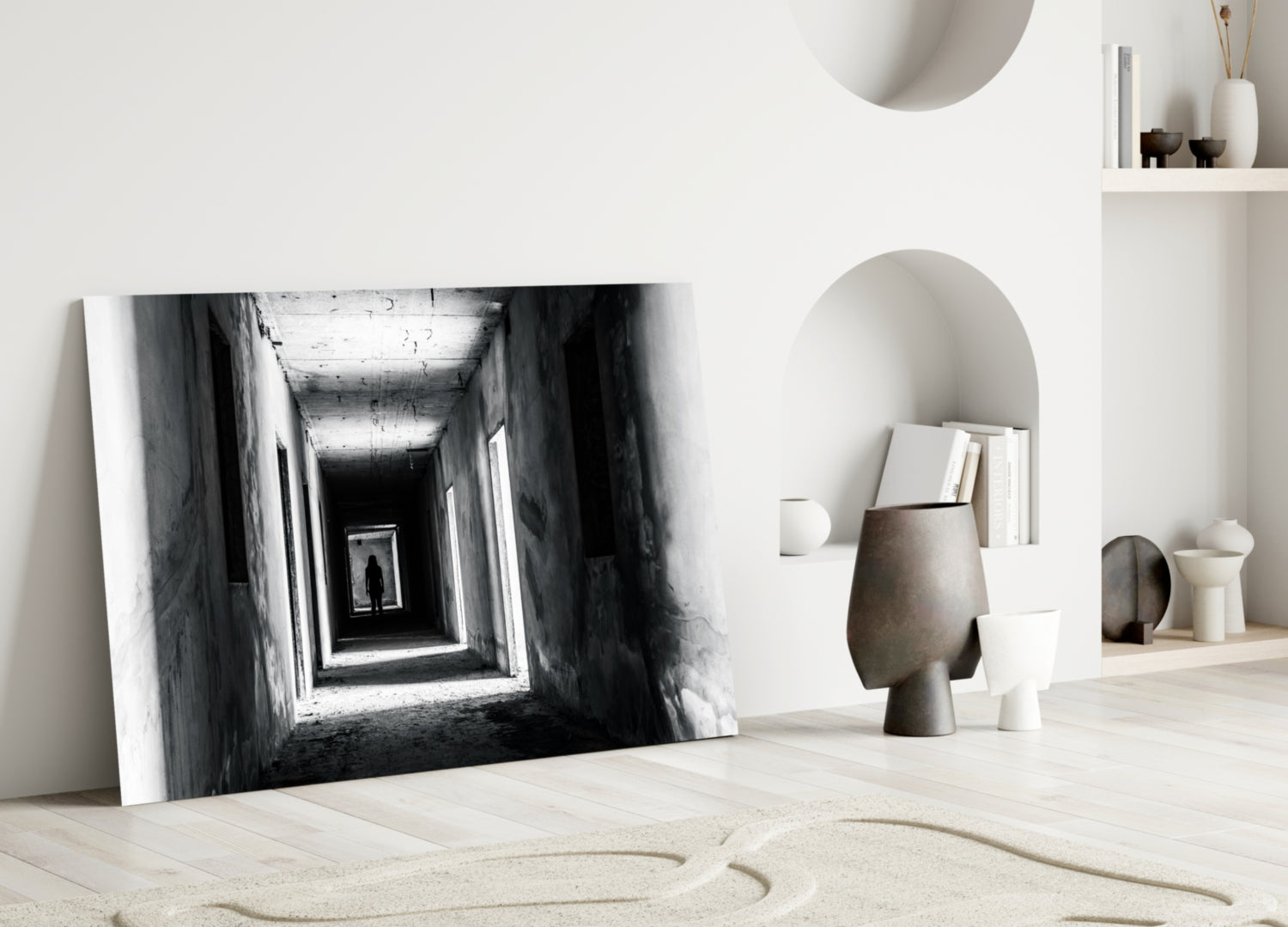 Black and white photograph of a tunnel with a distant silhouetted figure, leaning against white wall in minimalist interior setting.