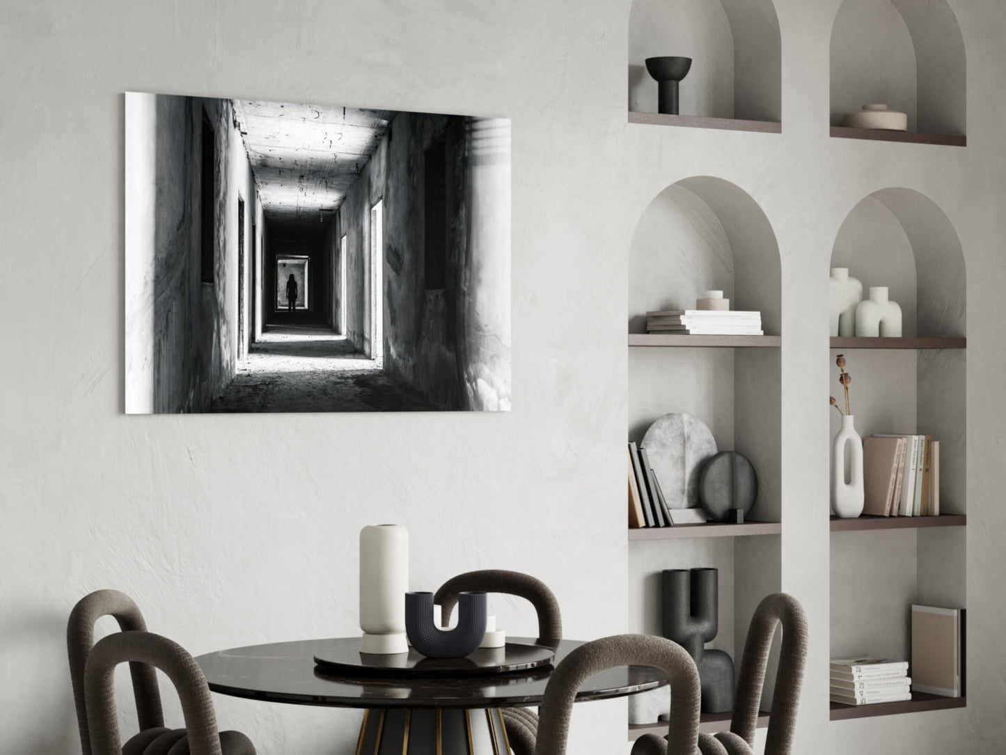 Black and white photograph of a receding tunnel with a solitary figure, displayed above a round black dining table with upholstered chairs and styled shelving.