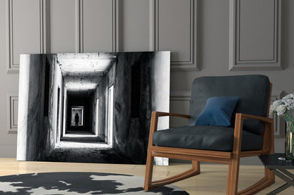 Black and white photograph of a receding tunnel with concrete walls displayed as glass wall art in a modern living room setting.