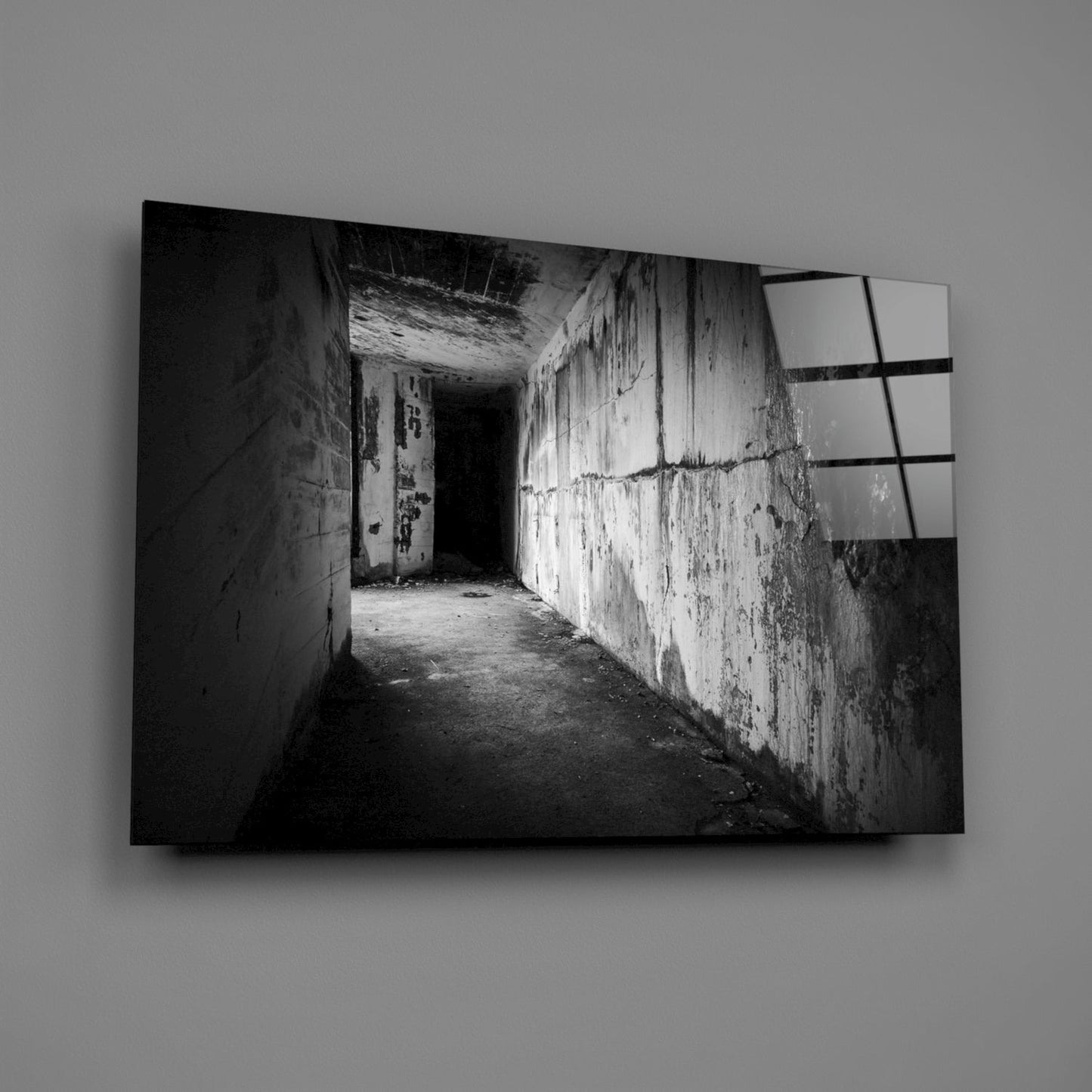 Black and white photograph of a deteriorating concrete hallway with peeling walls and gridded window visible on right side, printed on glass wall art panel.