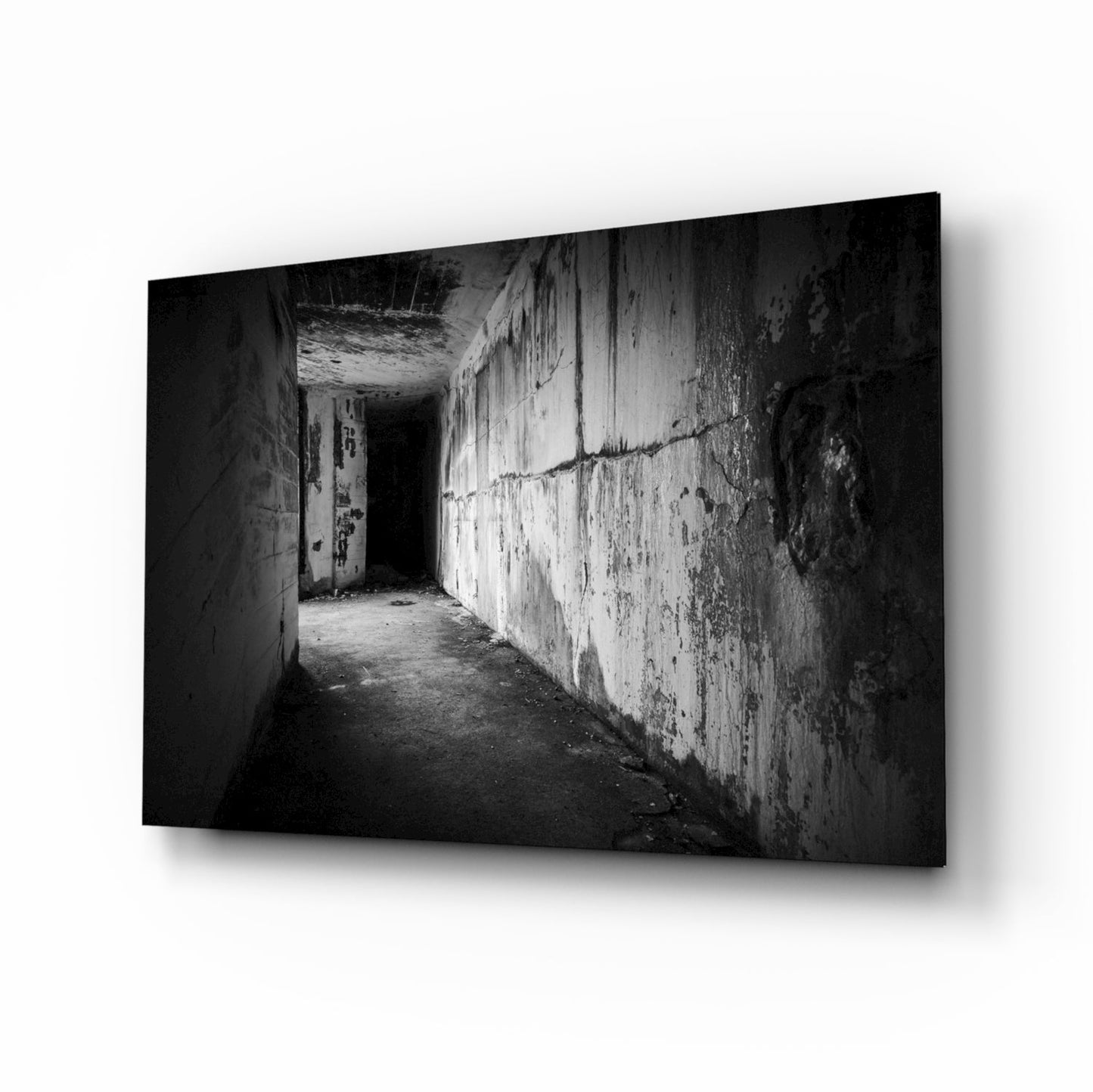 Black and white photograph of a deteriorating concrete hallway with peeling walls and an open doorway, displayed as a glass wall art panel.