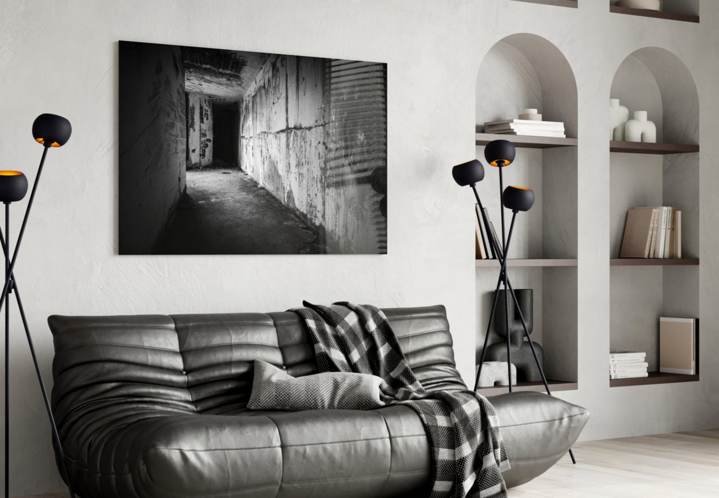 Black and white photograph of a deteriorating concrete corridor displayed as framed glass wall art above a gray leather sofa.
